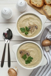 Delicious mushroom cream soup with parsley served on white wooden table, flat lay