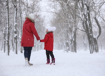 Photo of Mother with her child spending time outside on winter day, back view. Christmas vacation