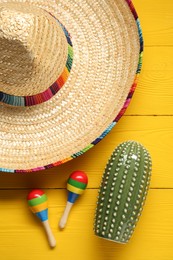 Mexican sombrero hat, maracas and toy cactus on yellow wooden background, flat lay