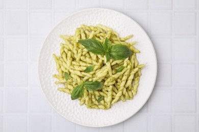 Photo of Plate of delicious trofie pasta with pesto sauce and basil leaves on white tiled table, top view