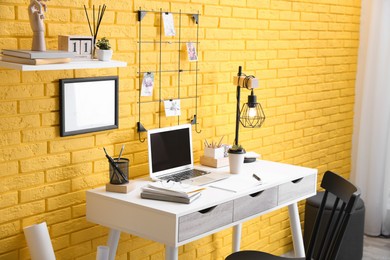 Stylish home office interior with comfortable workplace near yellow brick wall