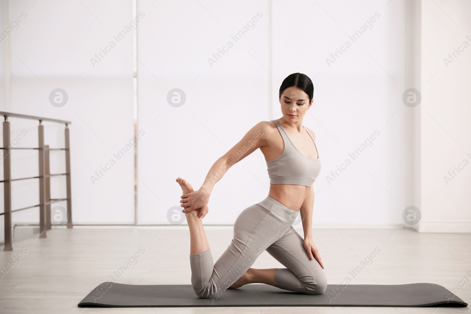 Photo of Young woman practicing One Legged King Pigeon asana in yoga studio. Eka Pada Rajakapotasana pose