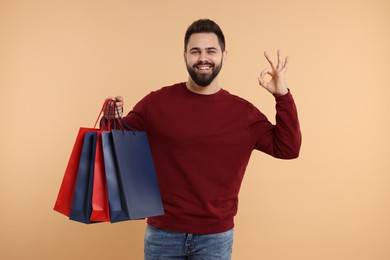 Smiling man with many paper shopping bags showing ok gesture on beige background