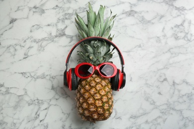 Photo of Pineapple with headphones and sunglasses on white marble background, top view. Creative concept