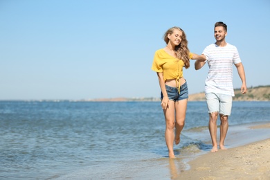 Happy young couple walking at beach on sunny day