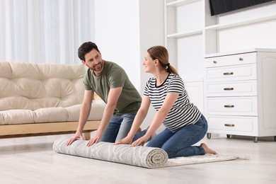 Photo of Smiling couple unrolling carpet with beautiful pattern on floor in room