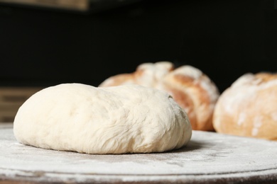 Wooden board with flour and bread dough on table against dark background. Space for text