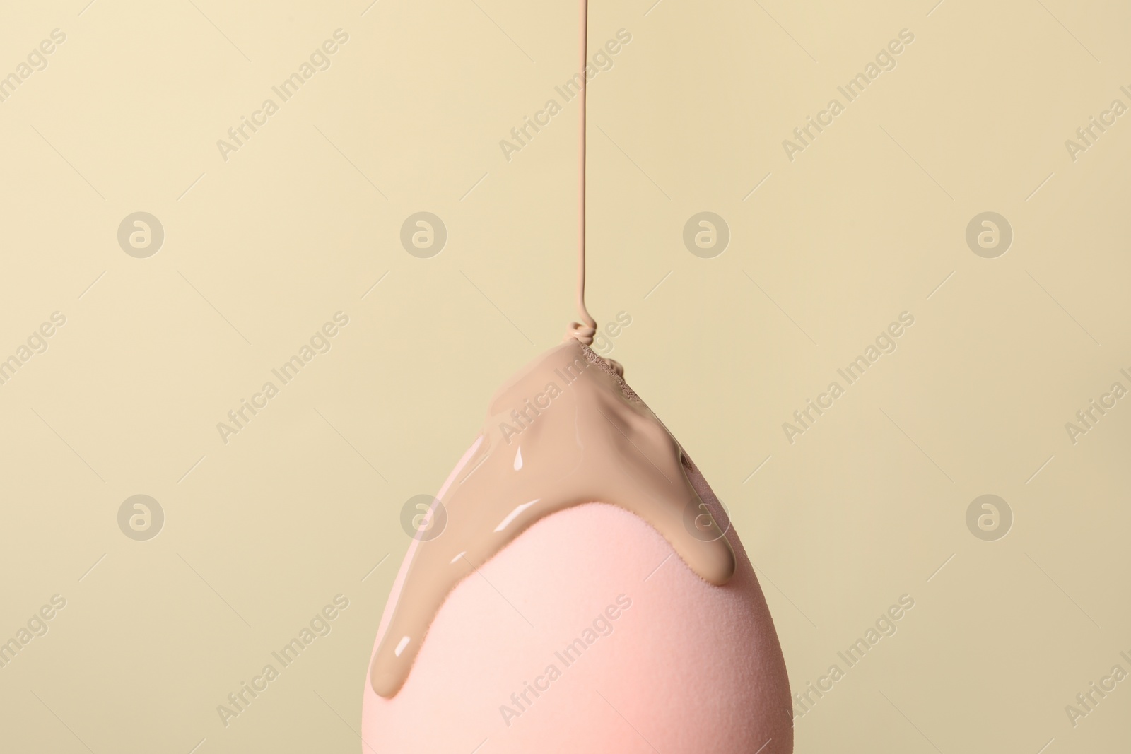 Photo of Skin foundation pouring onto makeup sponge on beige background