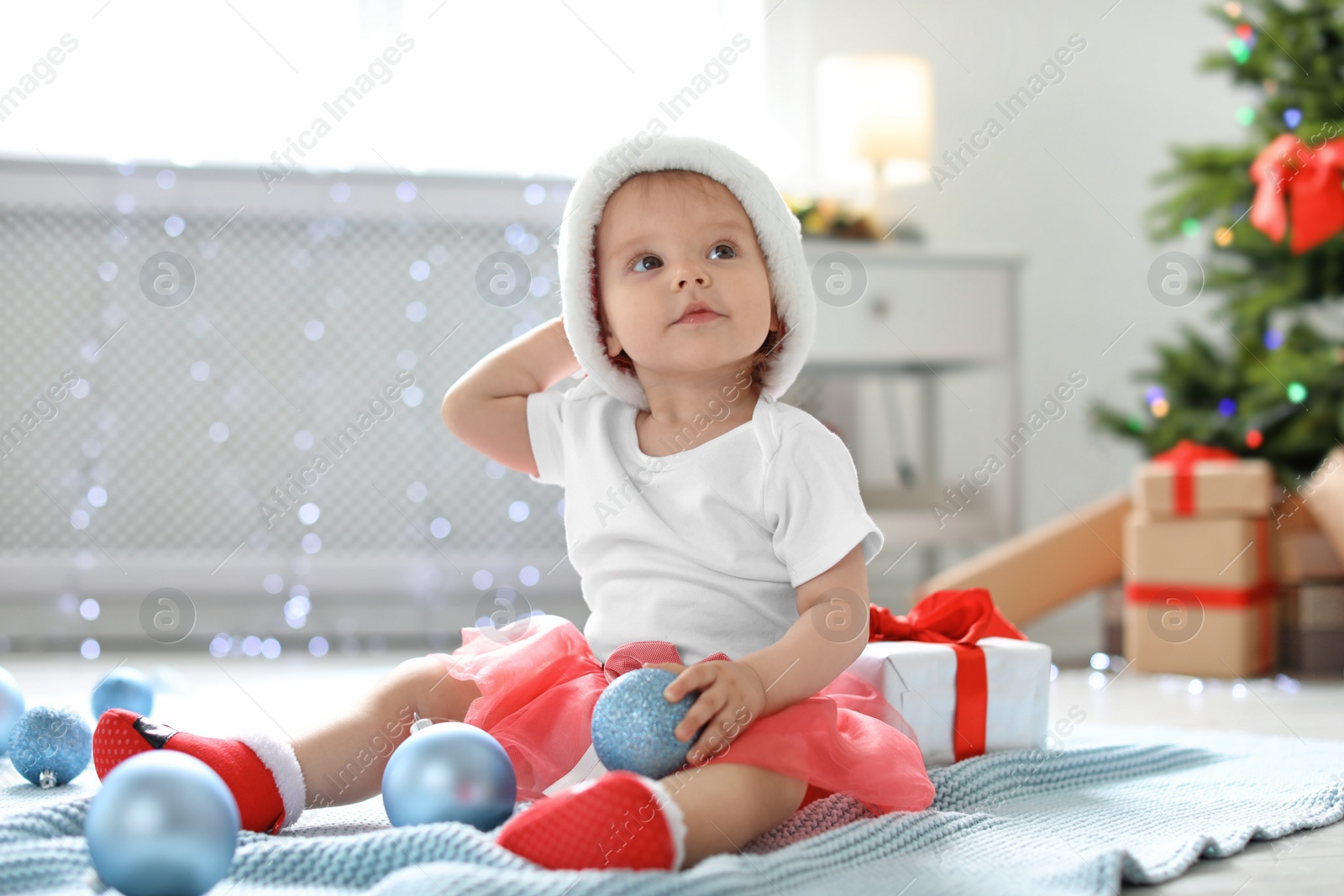 Photo of Cute baby in festive costume playing with Christmas decor on floor at home