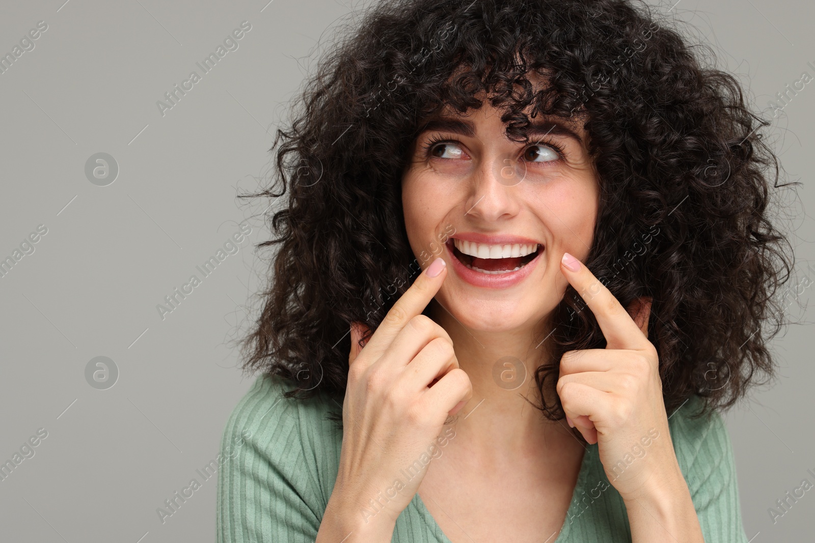 Photo of Young woman showing her teeth with whitening strip on grey background, space for text