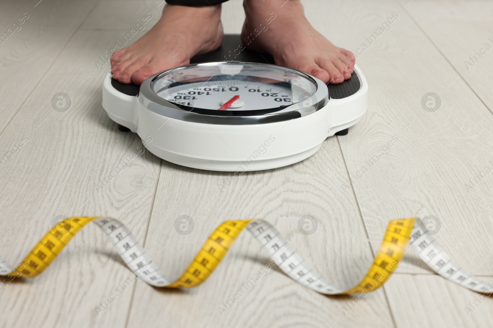 Photo of Woman using scales on floor near measuring tape, closeup. Overweight problem
