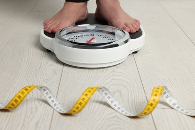 Woman using scales on floor near measuring tape, closeup. Overweight problem