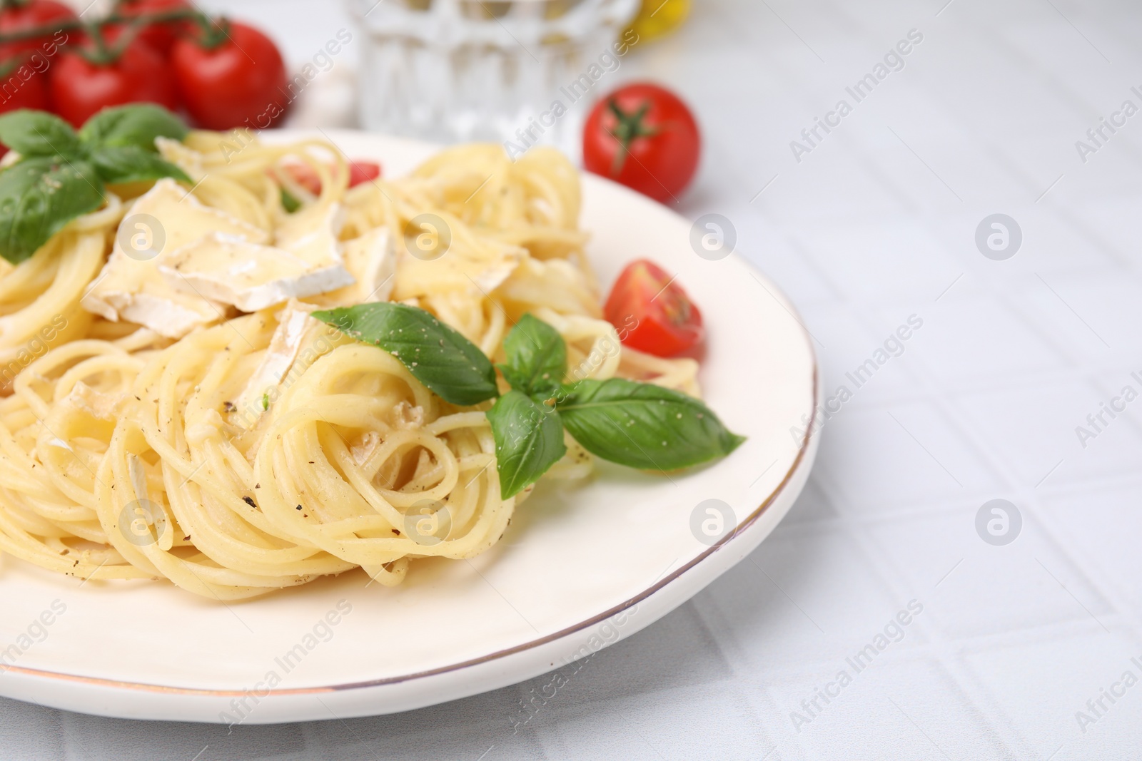 Photo of Delicious pasta with brie cheese, tomatoes and basil leaves on white tiled table, closeup. Space for text