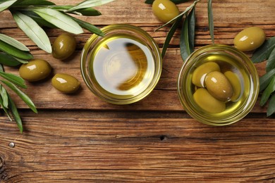 Photo of Bowls with cooking oil, green leaves and olives on wooden table, flat lay. Space for text