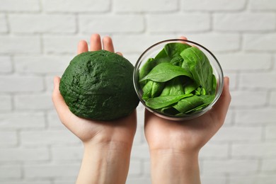 Photo of Woman holding dough painted with natural food coloring and spinach near white brick wall, closeup
