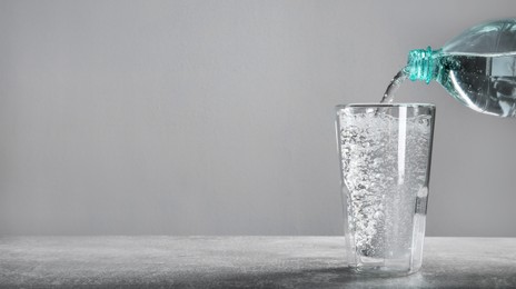 Pouring refreshing soda water into glass on gray table. Banner design with space for text