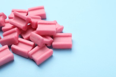 Photo of Tasty pink chewing gums on light blue background, space for text