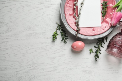 Festive Easter table setting with blank card on wooden background, top view. Space for text