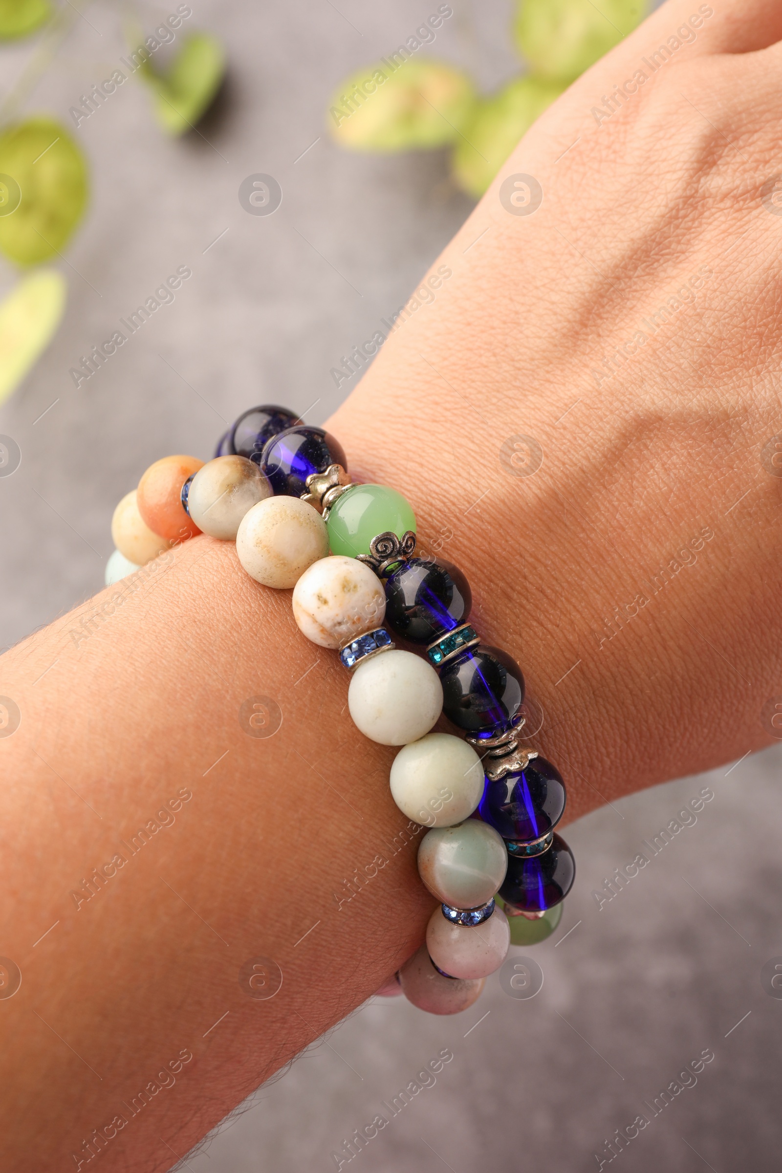 Photo of Woman wearing beautiful bracelets with gemstones on blurred background, closeup