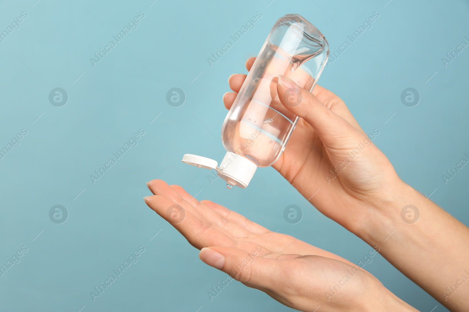 Photo of Woman applying antiseptic gel on light blue background, closeup