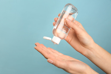 Woman applying antiseptic gel on light blue background, closeup