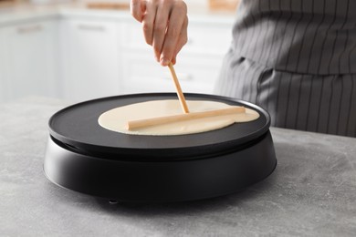 Photo of Woman cooking delicious crepe on electric pancake maker at table indoors, closeup