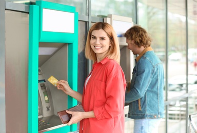 Beautiful woman with credit card near cash machine outdoors