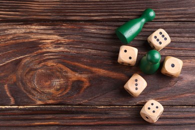Photo of Many dices and green game pieces on wooden table, flat lay. Space for text
