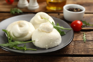 Photo of Delicious burrata cheese with arugula on wooden table, closeup