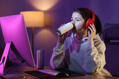 Girl with energy drink playing computer game at home