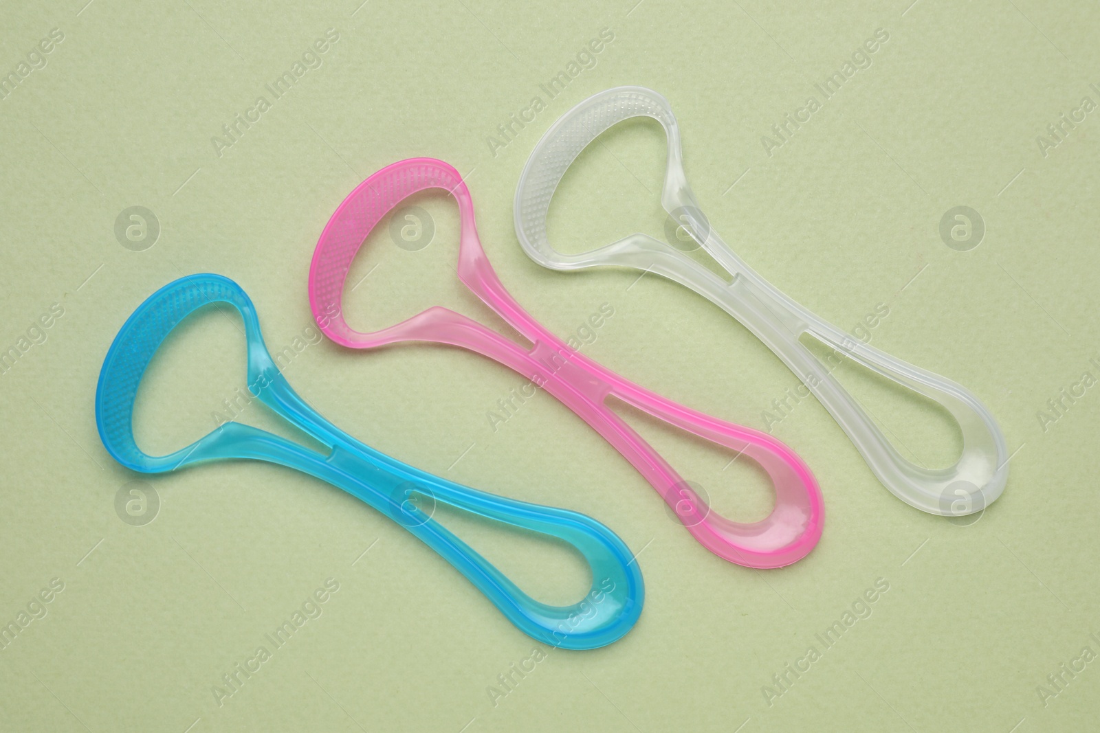 Photo of Colorful tongue cleaners on olive background, flat lay