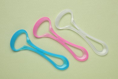 Photo of Colorful tongue cleaners on olive background, flat lay