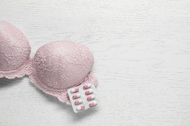 Photo of Breast cancer awareness. Bra and pills on white wooden table, top view. Space for text