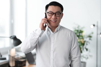 Portrait of smiling businessman talking by smartphone in office