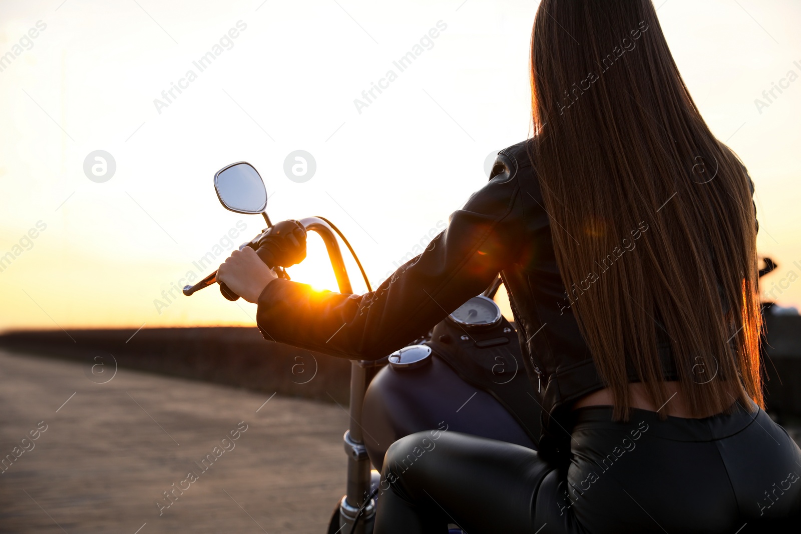 Photo of Woman riding motorcycle at sunset, back view. Space for text