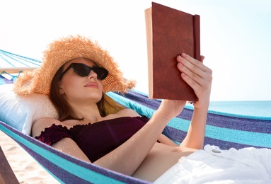 Photo of Young woman reading book in hammock on beach