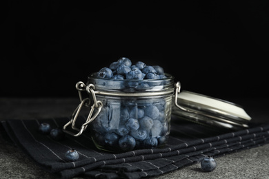 Tasty ripe blueberries in glass jar on grey table