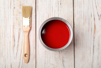 Photo of Can with red paint and brush on wooden background, top view