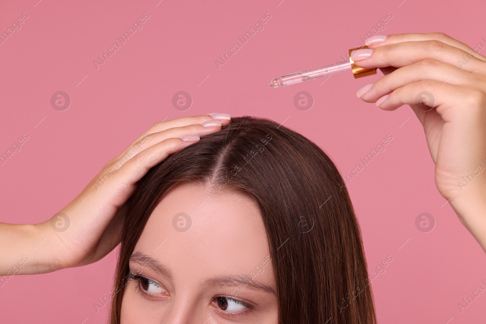 Photo of Woman applying serum onto hair on pink background, closeup