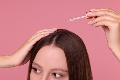 Photo of Woman applying serum onto hair on pink background, closeup