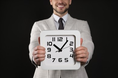 Photo of Happy businessman holding clock on black background, closeup. Time management