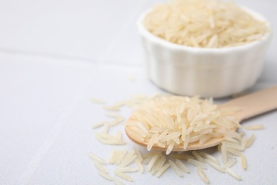 Wooden spoon with raw rice on white table, closeup. Space for text