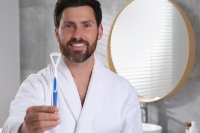 Happy man with tongue cleaner in bathroom, space for text