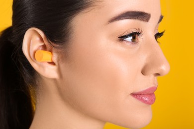 Young woman wearing foam ear plug on yellow background, closeup