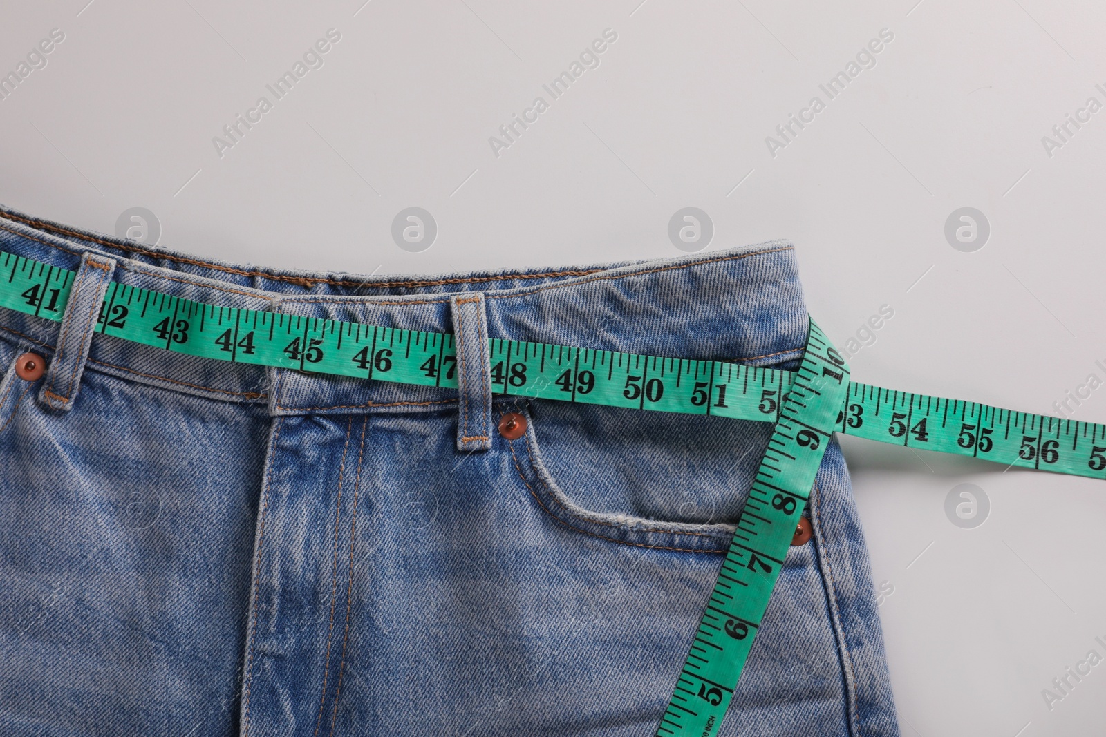 Photo of Jeans with measuring tape on light grey background, top view. Weight loss concept