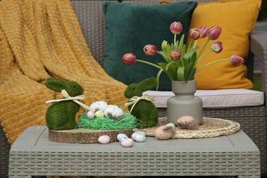 Terrace with Easter decorations. Bouquet of tulips in vase, bunny figures and decorated eggs on table outdoors