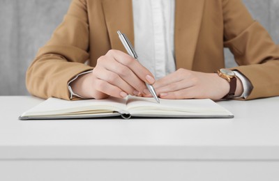 Woman writing with pen in notebook at white table, closeup