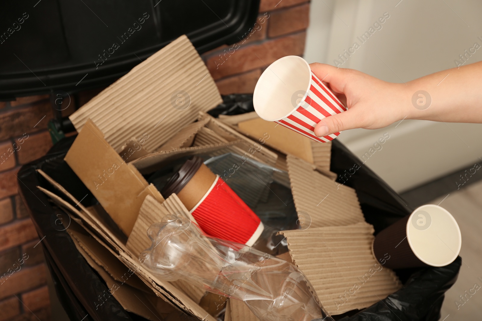 Photo of Young woman throwing popcorn cup in trash bin indoors, closeup. Waste recycling