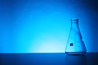 Photo of Empty conical flask on table against color background. Chemistry laboratory glassware