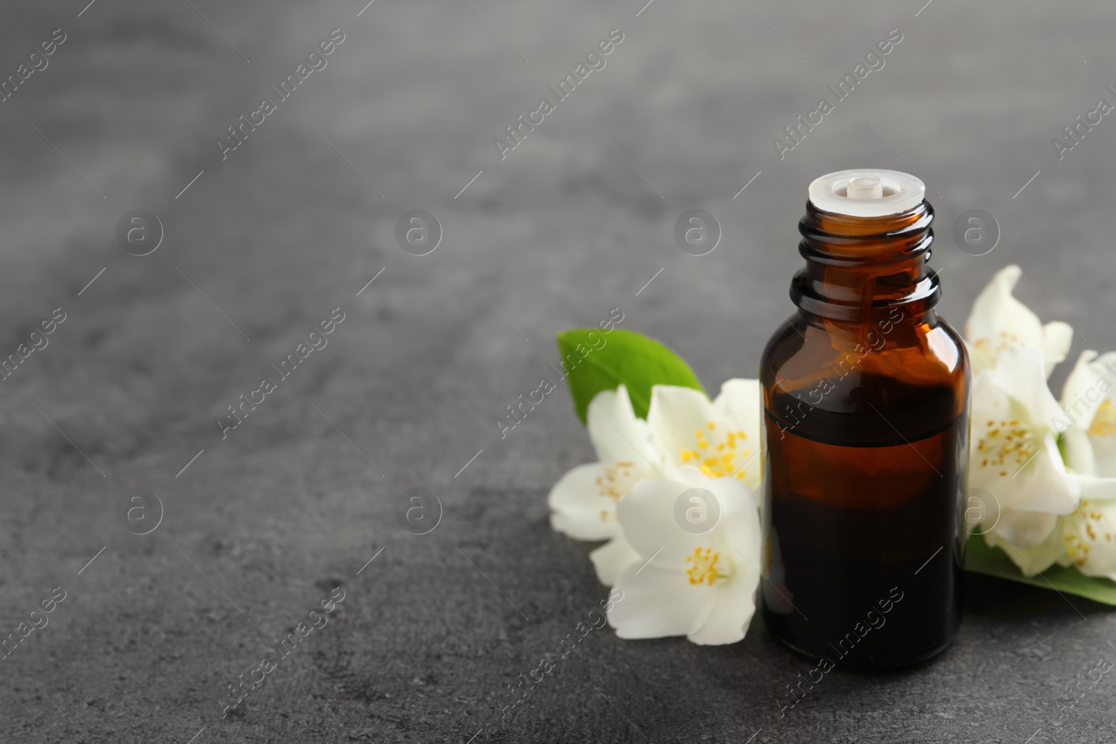 Photo of Essential oil and jasmine flowers on grey table. Space for text